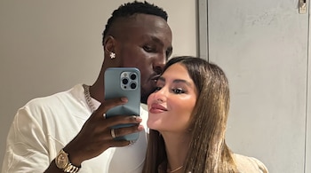 Primer plano de un hombre y una mujer tomándose una selfie con un teléfono móvil; el hombre besa la mejilla de la mujer.