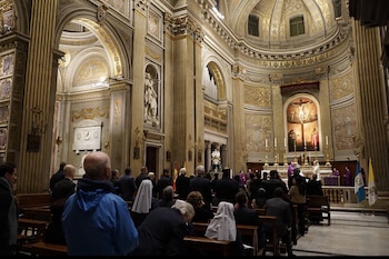 Vista interior de una iglesia barroca dorada con columnas, arcos y fieles sentados, frente a un altar con un crucifijo y sacerdotes, y banderas de Guatemala y el Vaticano