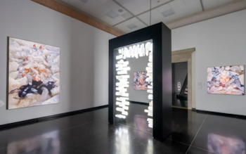 Sala de galería de arte con paredes claras y suelo oscuro. Tres cuadros con figuras humanas y cristales. Una instalación negra con luces blancas en el centro
