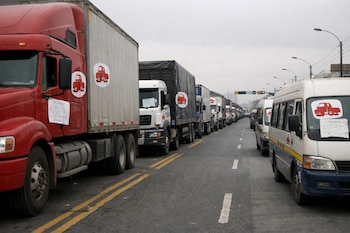 Avenida principal en Lima bloqueada por una fila de camiones, buses y combis. Los vehículos estacionados muestran logos de gremios y carteles de protesta.