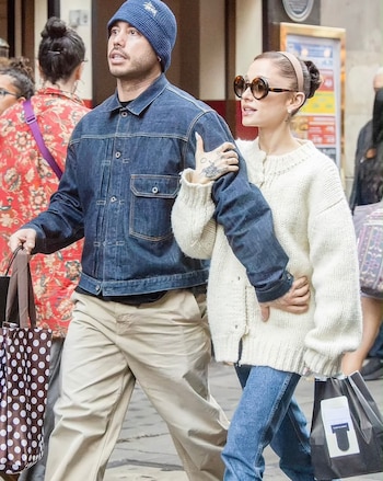 Ariana Grande camina junto a Ricky Alvarez en una calle mientras él viste una chaqueta de mezclilla y ella un suéter blanco