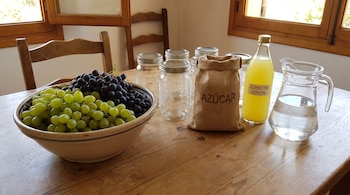 Un bol con uvas verdes y negras, varios tarros de vidrio, un saco de azúcar, una botella de zumo de limón y una jarra de agua sobre una mesa.
