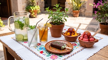 Jarra y vasos con hielo y limón, maceta con menta, una paleta de chocolate y dos vasijas de barro con nieve cubierta con chile.