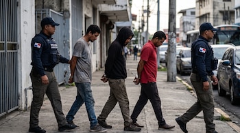 Tres hombres esposados caminan en fila escoltados por dos policías con uniformes que llevan la insignia de Panamá.