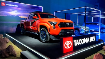 Una camioneta Toyota Tacoma de color naranja sobre una plataforma de exhibición junto a letreros luminosos con el nombre del modelo