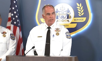 Un oficial de la policía de Filadelfia en uniforme blanco habla ante un micrófono frente a un escudo policial y la bandera de Estados Unidos