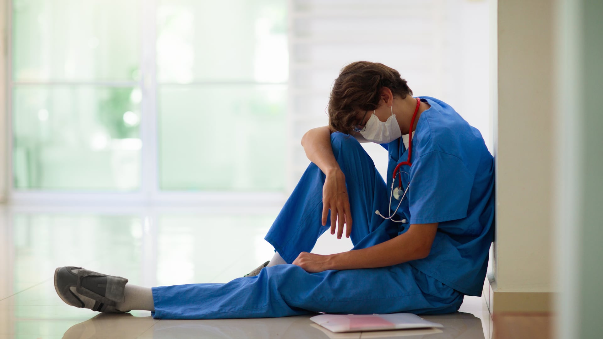 Un médico joven, visiblemente cansado, se sienta en el suelo de un hospital. (Canva)
