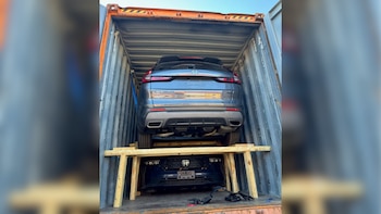 Dos SUVs Honda CR-V grises apilados dentro de un contenedor de envío de metal naranja y gris, sujetados con correas azules y una estructura de madera