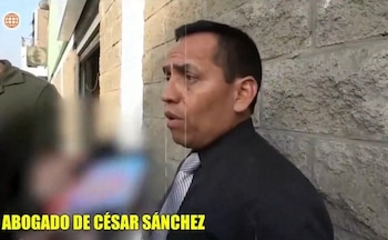 Hombre de tez morena, con camisa oscura y corbata rayada, habla frente a una pared de bloques. Un rótulo amarillo lo identifica como abogado de César Sánchez