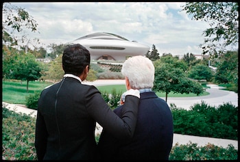 Vista trasera de Mellody Hobson con chaqueta negra y George Lucas con chaqueta oscura, mirando el Lucas Museum of Narrative Art. El edificio es blanco, ovalado, con paisaje verde