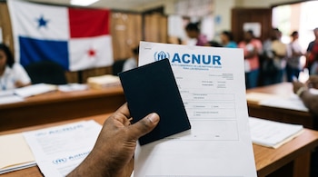 Una mano sostiene un pasaporte oscuro y un documento del ACNUR en una sala con mesas y una bandera de Panamá en la pared.