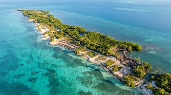 Vista aérea de una isla estrecha con vegetación verde, franjas de tierra nivelada y agua turquesa del mar Caribe.