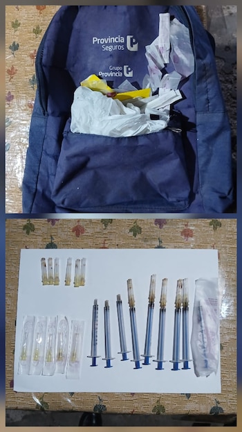 Varias jeringas plásticas, agujas hipodérmicas en sus empaques, una caja de clenbuterol y el borde de una computadora portátil sobre un mantel