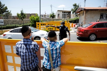 Jóvenes observan cómo un policía israelí trabaja en la entrada del asentamiento judío de Beitar Illit, que Israel ha declarado zona restringida después de un aumento en los casos de la nueva enfermedad por coronavirus (COVID-19), en la zona occidental ocupada por Israel.. REUTERS/Ronen Zvulun/File Photo