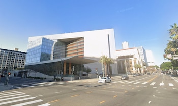 Edificio moderno de fachada de cristal y muros blancos en una esquina con cruce peatonal, semáforos, vehículos y palmeras