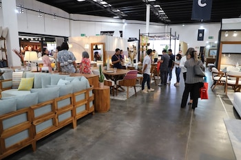 Varias personas transitan por los pasillos de una exposición, observando sofás, mesas, sillas, lámparas y decoraciones en distintos stands