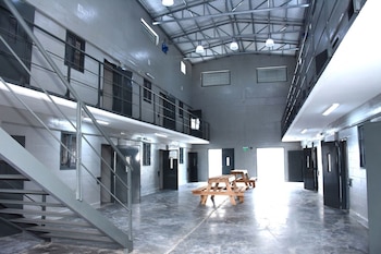 Interior de un pabellón penitenciario con puertas de celdas en dos niveles, escaleras metálicas y mesas de madera en la zona central