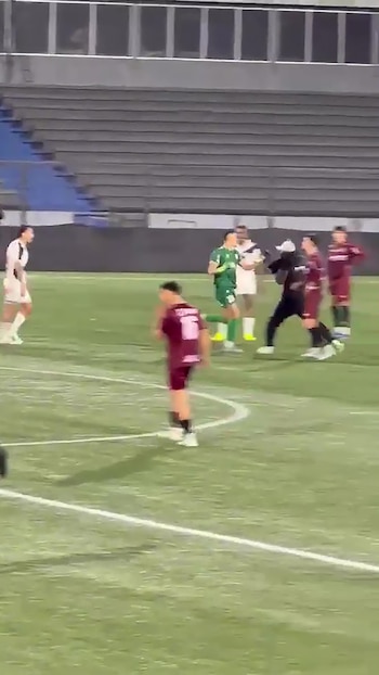 Futbolistas con uniformes deportivos y un individuo en ropa oscura se encuentran en la cancha de un estadio