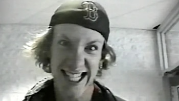 Primer plano de Dylan Klebold sonriendo con una gorra oscura de béisbol con logo 'B', cabello claro y ojos intensos, en una imagen en escala de grises