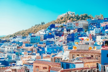 Edificios pintados de azul con tejados de teja sobre la ladera de una colina arbolada bajo un cielo despejado