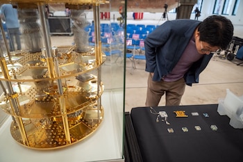 Un hombre con gafas mira varios microchips colocados sobre una mesa negra junto a un cilindro dorado dentro de una vitrina