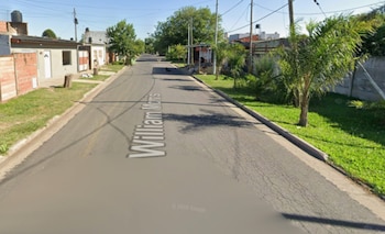 Calle residencial William Morris con asfalto, veredas de pasto, árboles, casas bajas a los lados y cielo azul claro en un día soleado