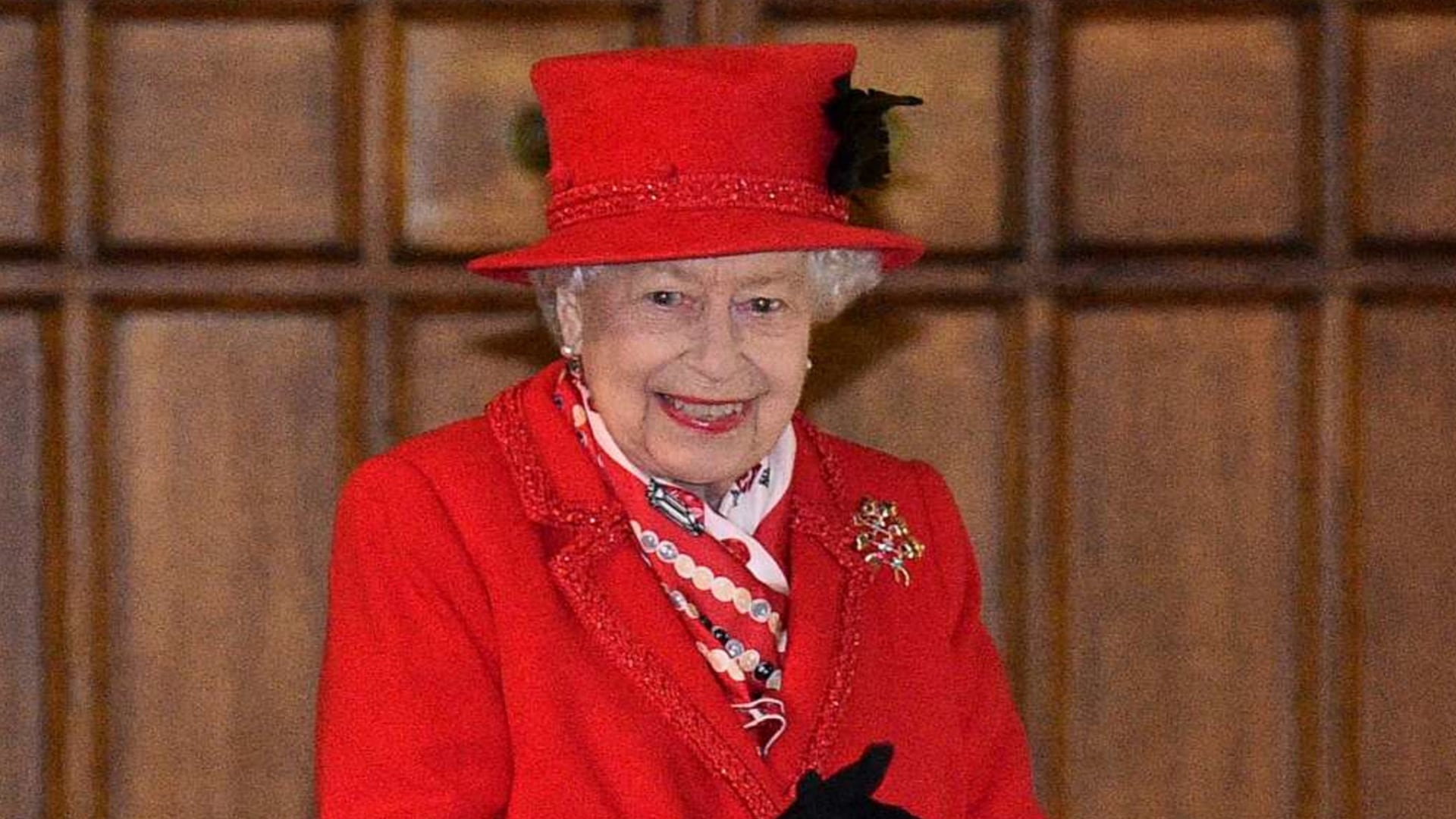 Conjunto monocromático rojo vibrante, abrigo con pasamanería, sombrero tipo caja y foulard estampado, junto a broche dorado y labios rojos (Glyn Kirk/Pool via AP)