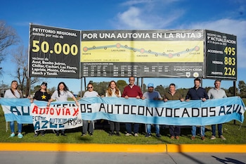 Un grupo de personas sostiene una pancarta que reclama una autovía frente a un cartel publicitario sobre la Ruta 3