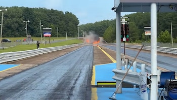 Pista de carreras de automovilismo. Incendio con humo y llamas en la distancia, semáforo de salida, barreras de seguridad y espectadores
