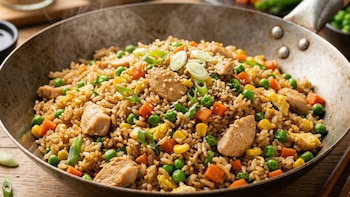 Primer plano de arroz frito caliente en un wok, con pollo, guisantes, zanahoria, maíz, huevo, cebolla verde y semillas de sésamo