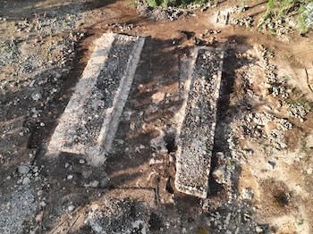 Vista aérea de un sitio arqueológico mostrando dos estructuras rectangulares paralelas hechas de piedra y rellenas de grava, sobre un terreno terroso con rocas