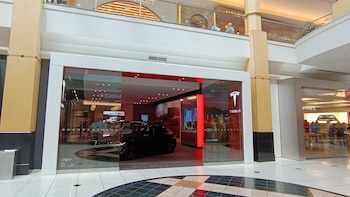 Fachada de cristal de un local de Tesla con automóviles exhibidos en su interior iluminado dentro de un centro comercial