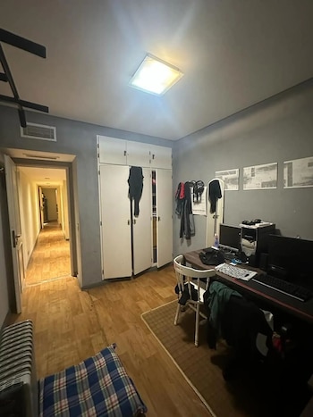 Habitación interior con suelo de parquet, paredes grises, un escritorio con dos monitores y computador, armario blanco y un pasillo iluminado al fondo