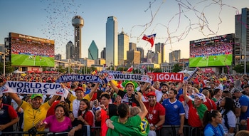 Multitud en Dallas celebra el Mundial. Confeti y bufandas. Pantallas de fútbol y skyline de la ciudad con la Reunion Tower al fondo.