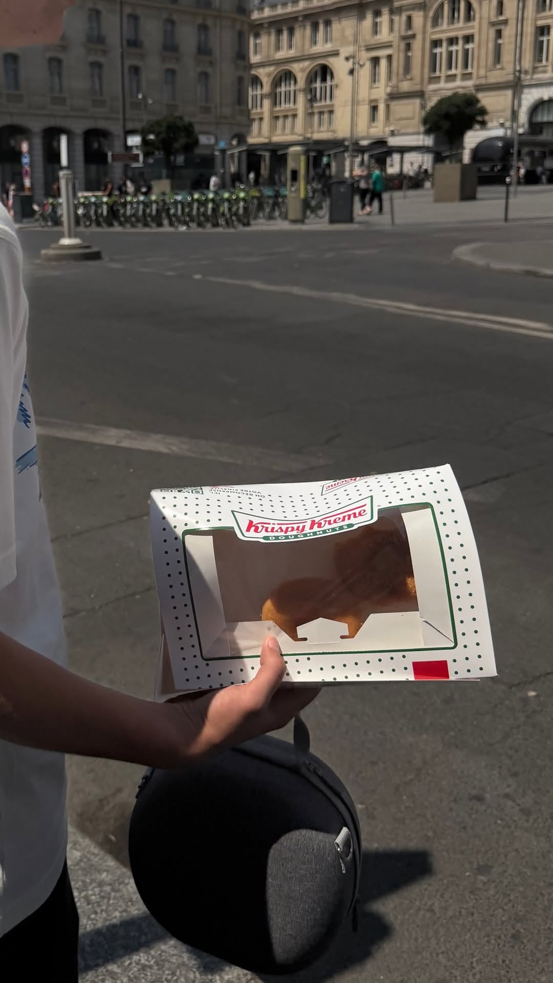 Uno de los hijos de la conductora sostiene una caja de Krispy Kreme Doughnuts en las calles de París, con la arquitectura de la ciudad como fondo