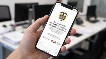 Mano sosteniendo un teléfono móvil que muestra en pantalla un documento con el escudo de Colombia y textos sobre la Ley 400 de 1997.