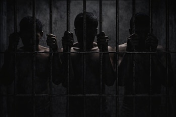 Tres siluetas de personas adultas sosteniendo barrotes metálicos frente a un muro de hormigón en un entorno oscuro.