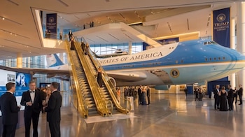 Sala de exposición de la Biblioteca Presidencial Trump con una réplica de Air Force One, un helicóptero presidencial, escaleras mecánicas doradas y asistentes formales