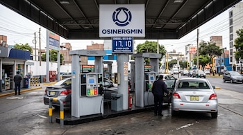 Surtidores de combustible con vehículos estacionados, un tablero con precios digitales y un letrero de Osinergmin en una estación de servicio.