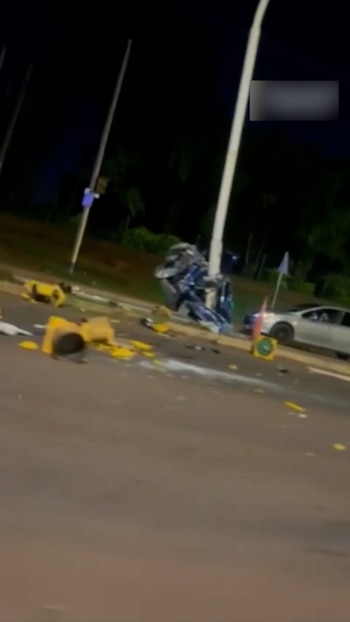 Una camioneta azul destrozada tras chocar contra un poste en una carretera oscura por la noche, con restos del vehículo y barreras de tráfico en el suelo