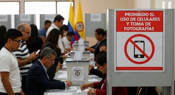 Cartel blanco y rojo que prohíbe el uso de celulares y la toma de fotografías, con un ícono de teléfono tachado, en un centro de votación en Colombia.