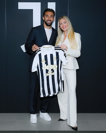 Un hombre con traje oscuro y una mujer con traje blanco sostienen una camiseta de fútbol a rayas de la Juventus frente a un fondo negro