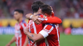 Dos futbolistas con camisetas de rayas rojas y blancas se abrazan de espaldas a la cámara.