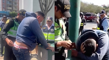 Un hombre con capucha azul permanece inclinado mientras agentes de policía con chalecos amarillos lo revisan en la vía pública