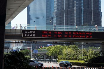 FOTO DE ARCHIVO: Transeúntes pasan por un paso elevado con una exhibición de información bursátil frente a edificios en el distrito financiero de Lujiazui en Shanghai, China, el 6 de agosto de 2024 (Reuters)