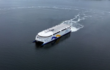 Un ferri catamarán blanco y azul de la empresa Buquebus navega en el agua con una estela de espuma detrás