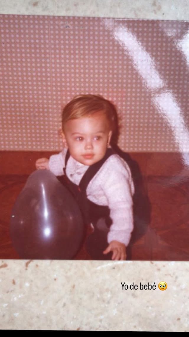Evangelina Anderson de bebé aparece en una imagen retro, sentada adorablemente junto a un globo oscuro frente a una pared rosa con lunares blancos (Instagram)