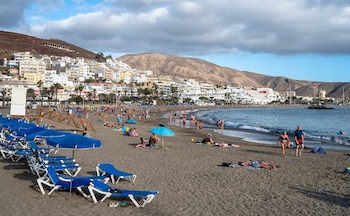 una playa, gente, sombrillas, el pueblo de fondo