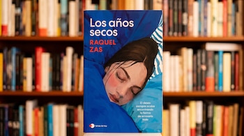 El libro Los años secos de Raquel Zas frente a estantes de madera llenos de libros desenfocados.
