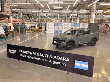 Una camioneta gris estacionada en una fábrica con un cartel negro que muestra la bandera de Argentina y el logotipo de Renault